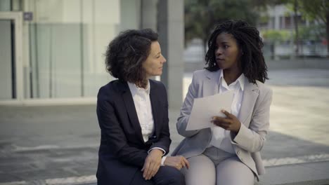 Serious-businesswomen-sitting-on-street-and-discussing-contract